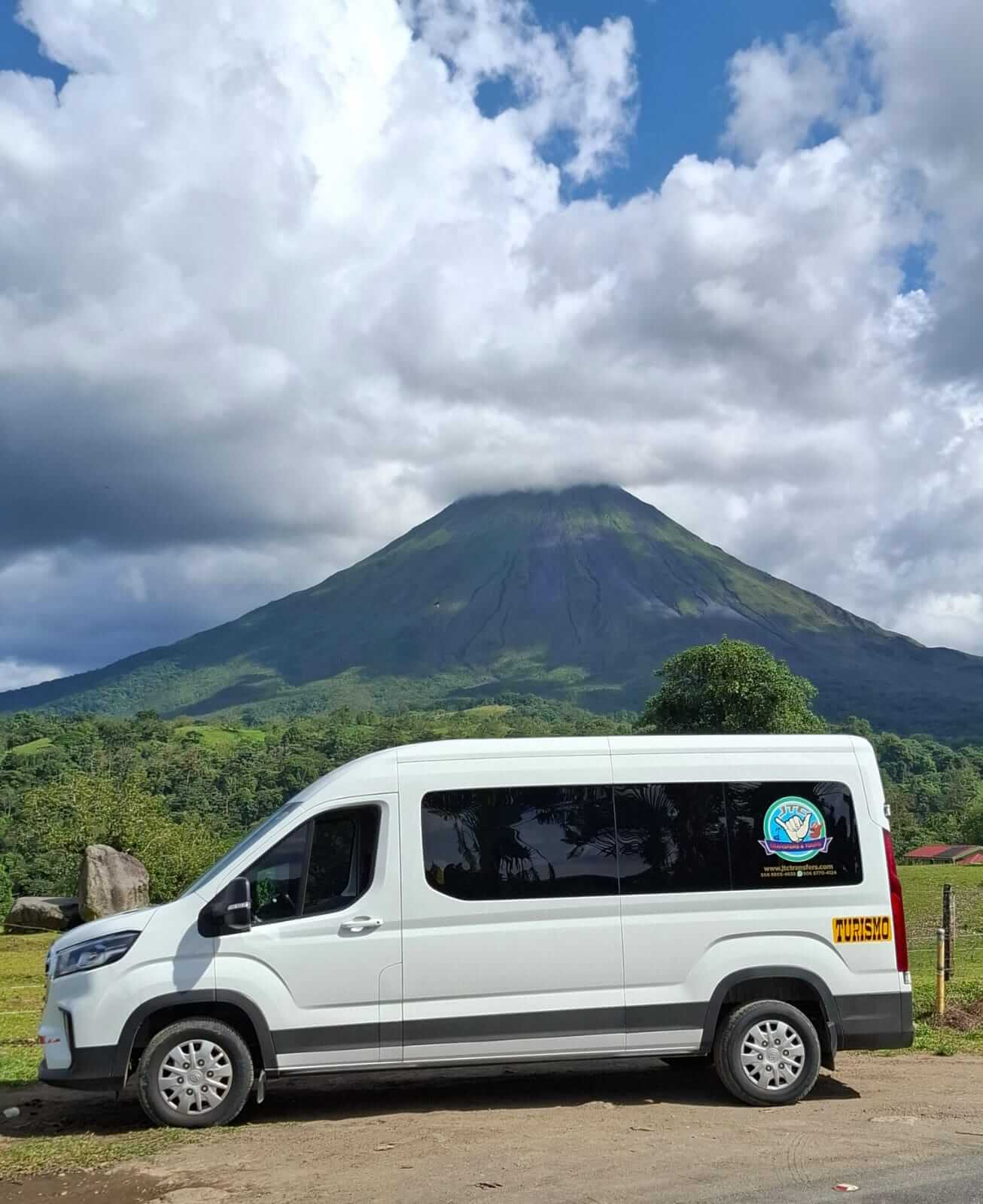 White JTC Transfer van offering Private Costa Rica airport transportation service. Parked with Arenal Volcano in the background