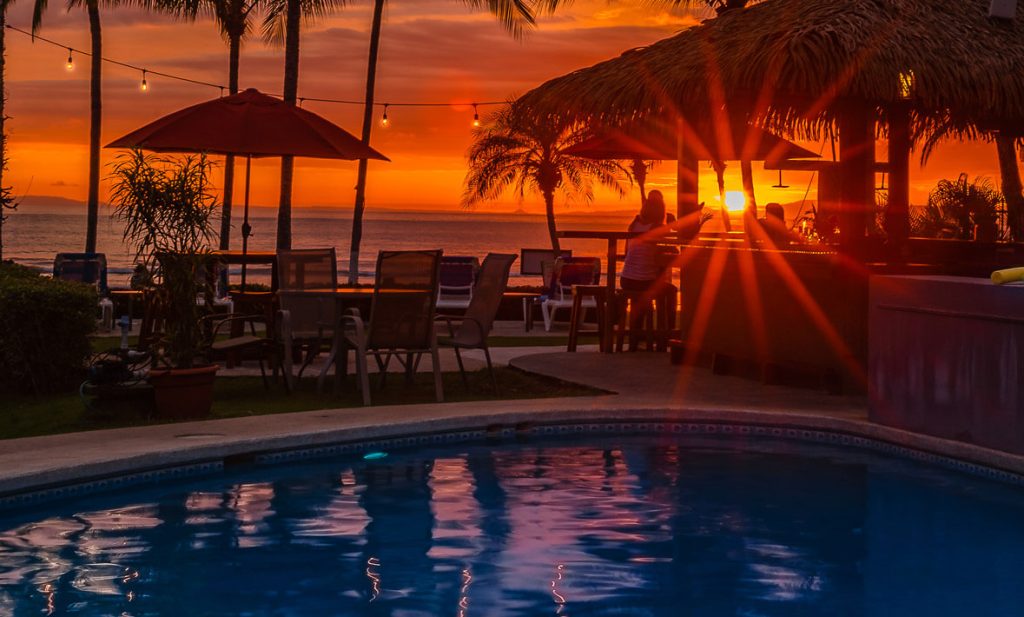 Sunset view at Hotel Club Del Mar in Jaco, Costa Rica with pool, beachfront bar, and palm trees by the ocean
