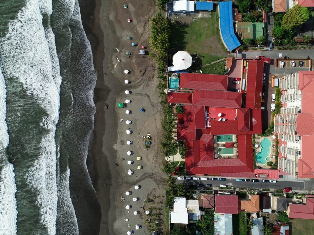 Aerial view of Hotel Cocal and Casino in Jaco, Costa Rica with beachfront access, swimming pools, and waves breaking on the shore