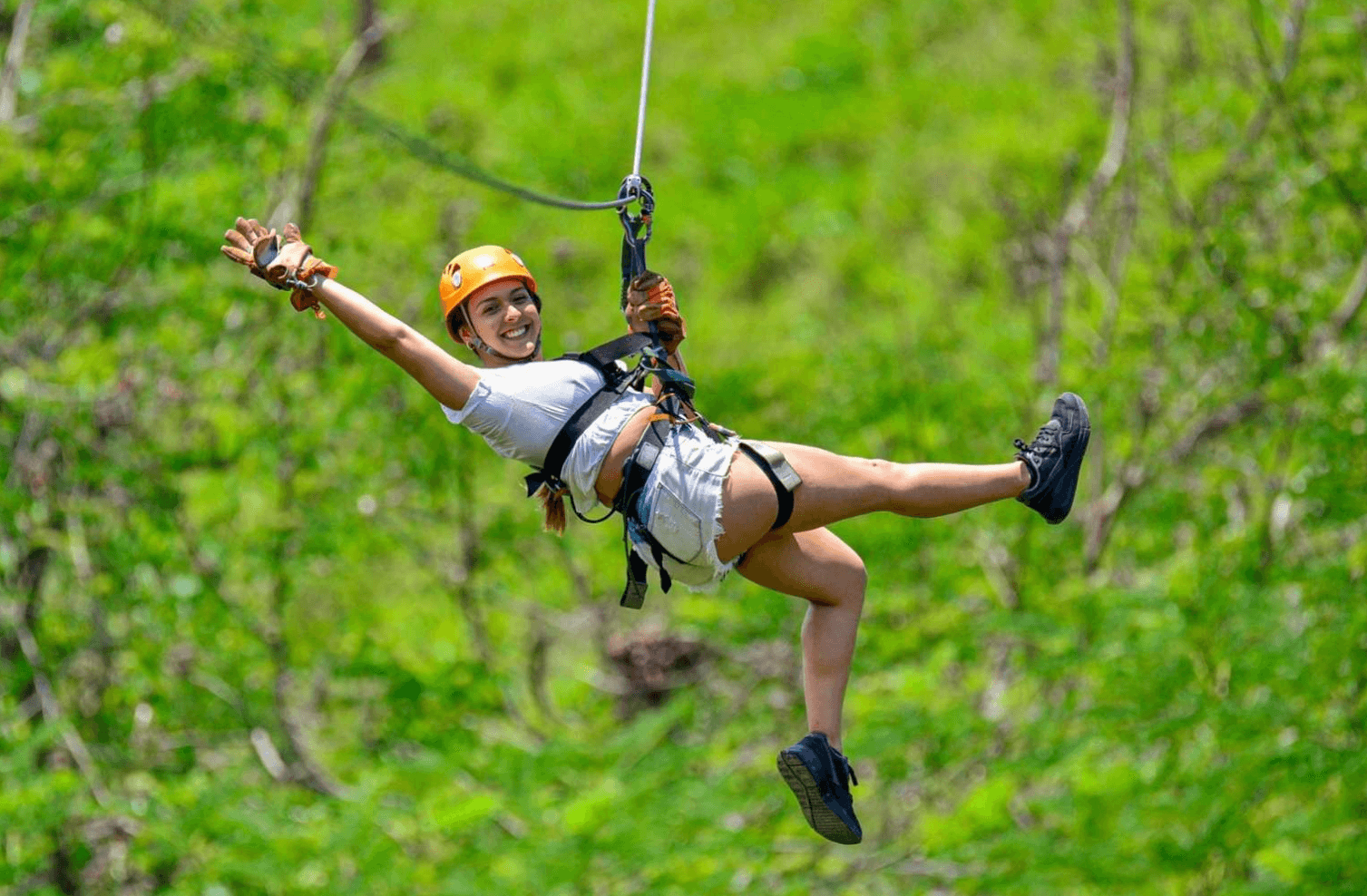 http://Smiling%20woman%20wearing%20helmet%20and%20harness%20ziplining%20above%20dense%20Costa%20Rica%20rainforest%20canopy%20during%20a%20canopy/zipline%20adventure%20near%20Jaco%20beach